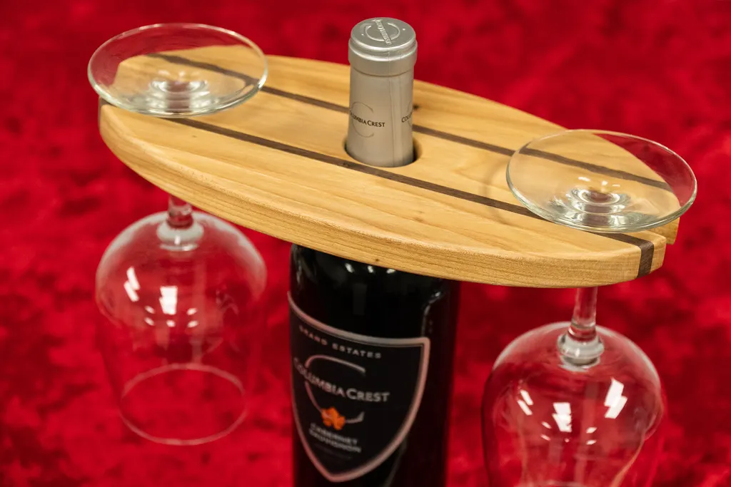 A personalized wooden wine caddy resting on a wine bottle and holding two wine glasses.