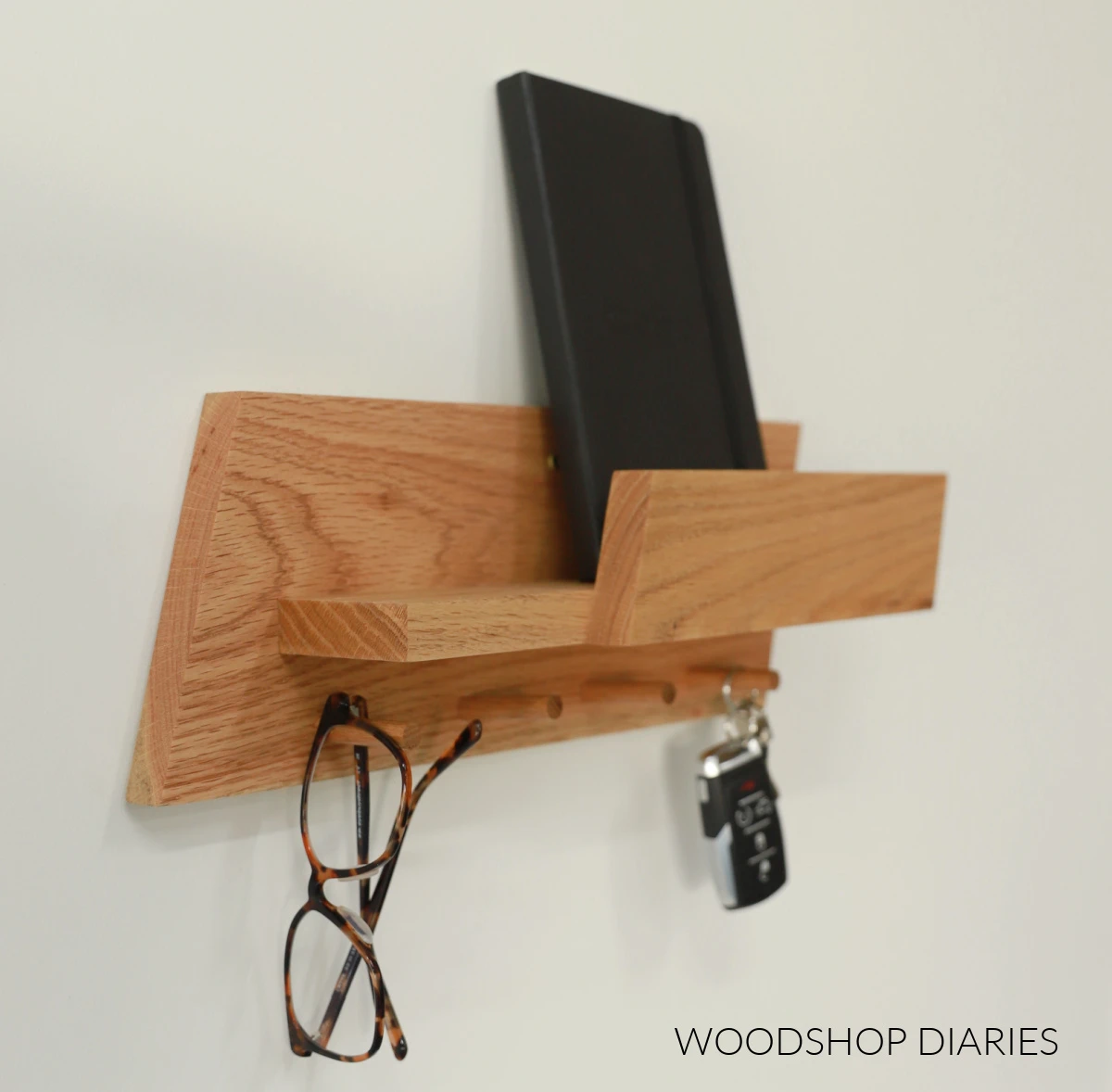 A modern scrap wood entryway shelf with wooden dowel pegs holding keys and sunglasses.